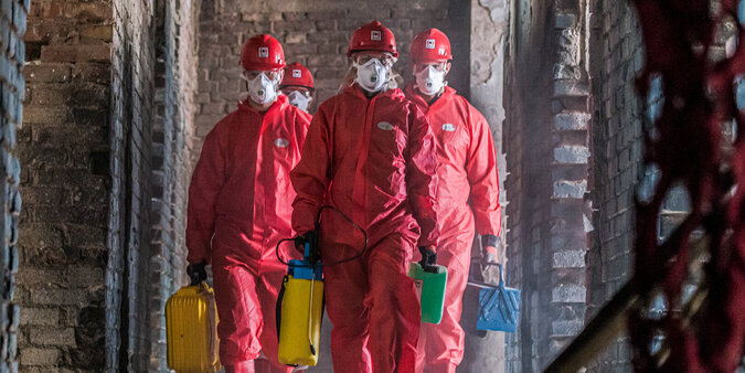 BELFOR Mitarbeiter  in roten Schutzanzügen mit Masken auf ihrem Job auf einer Baustelle.