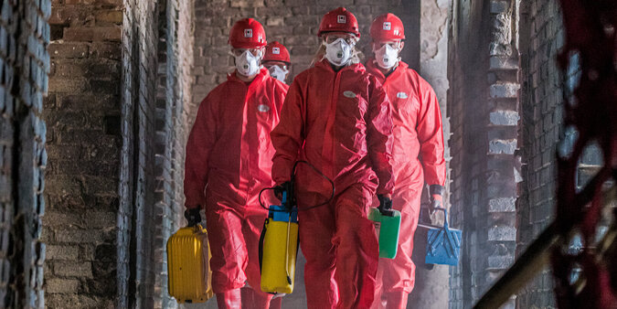 BELFOR - Bereit für Belfor BELFOR-medarbetare  i röda skyddsdräkter med masker på sitt arbete på en byggarbetsplats.