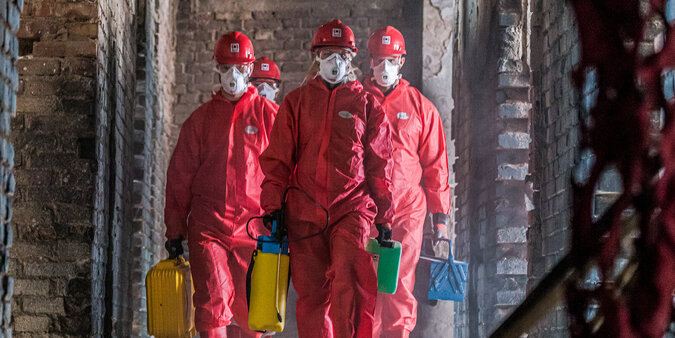 BELFOR Mitarbeiter  in roten Schutzanzügen mit Masken auf ihrem Job auf einer Baustelle.