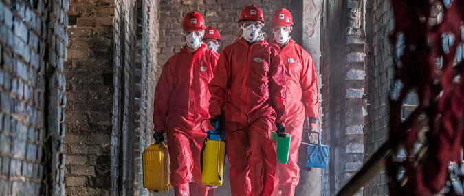 BELFOR Mitarbeiter  in roten Schutzanzügen mit Masken auf ihrem Job auf einer Baustelle.