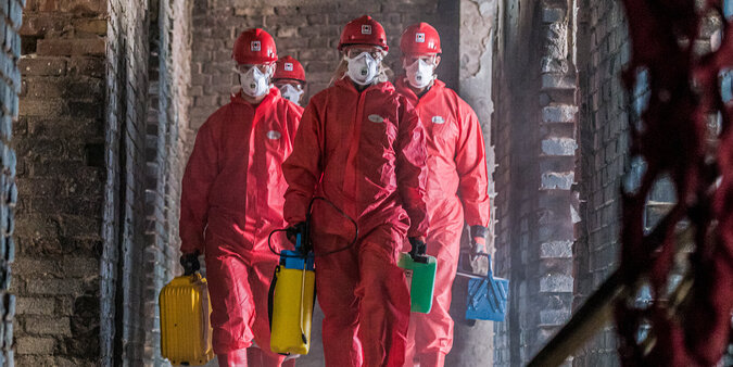 BELFOR Mitarbeiter  in roten Schutzanzügen mit Masken auf ihrem Job auf einer Baustelle.