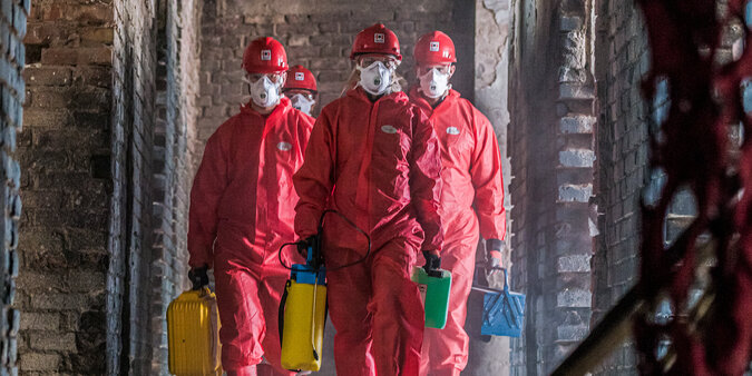 BELFOR Mitarbeiter  in roten Schutzanzügen mit Masken auf ihrem Job auf einer Baustelle.