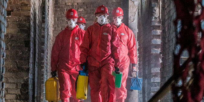 BELFOR Mitarbeiter  in roten Schutzanzügen mit Masken auf ihrem Job auf einer Baustelle.