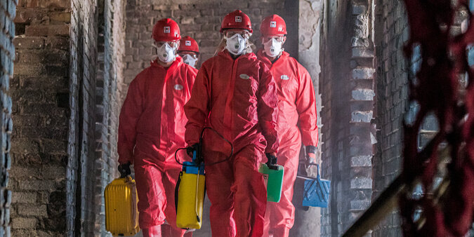 BELFOR - Bereit für Belfor BELFOR Mitarbeiter  in roten Schutzanzügen mit Masken auf ihrem Job auf einer Baustelle.