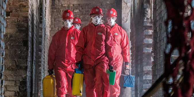 BELFOR Mitarbeiter  in roten Schutzanzügen mit Masken auf ihrem Job auf einer Baustelle.