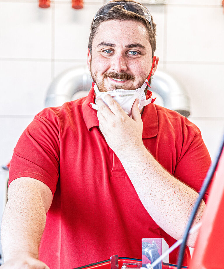 Arbeiter mit roten Shirt lächelt in Kamera und hat Staubschutzmaske heruntergezogen