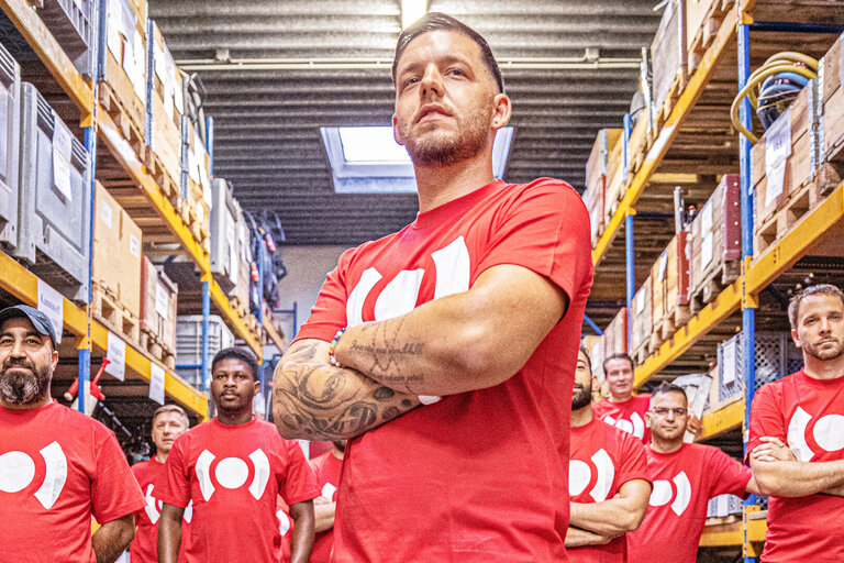 Gruppe von BELFOR Kollegen in Arbeitskleidung zeigt Teamgeist in einer Halle.