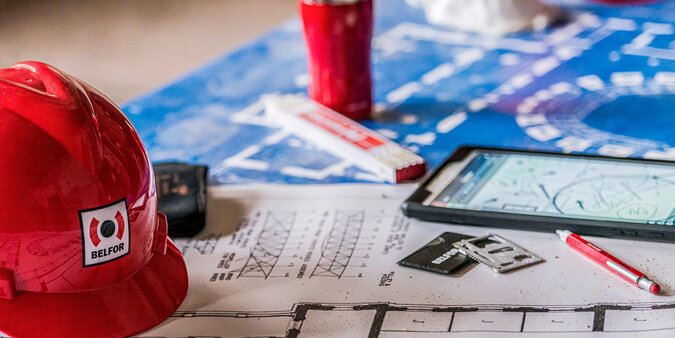 Werkplek met bouwhelm, plattegrond, pen en koffiemok